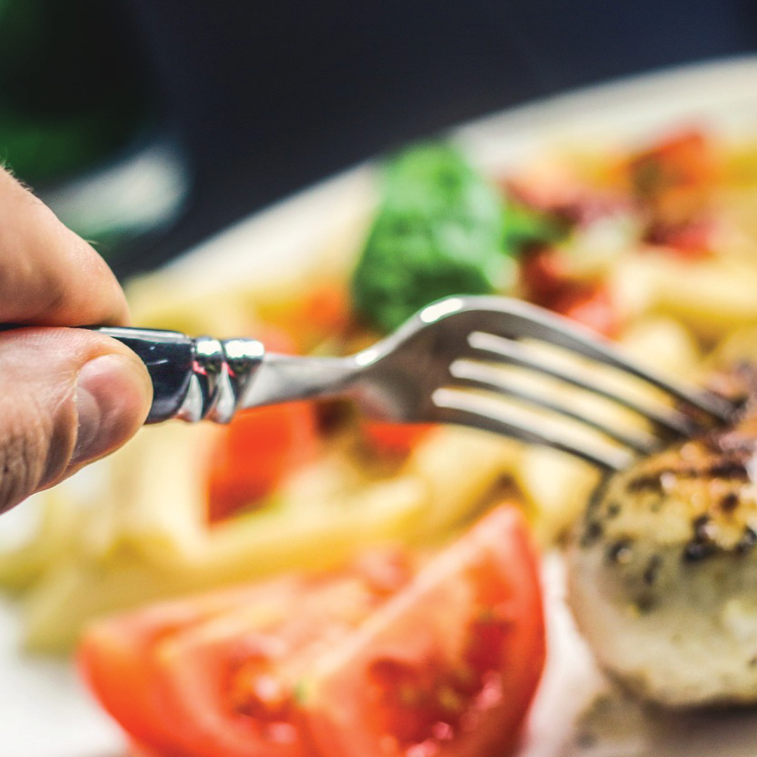 A hand holding a fork picks up a piece of chicken on a plate